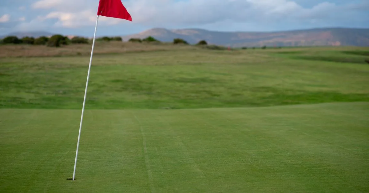 A beautiful golf course with a red flag on the green during a clear day.