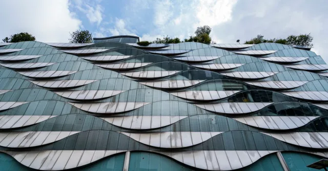 Futuristic building facade with wave-like glass patterns and greenery on top.