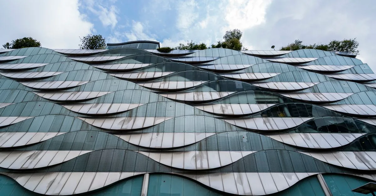 Futuristic building facade with wave-like glass patterns and greenery on top.