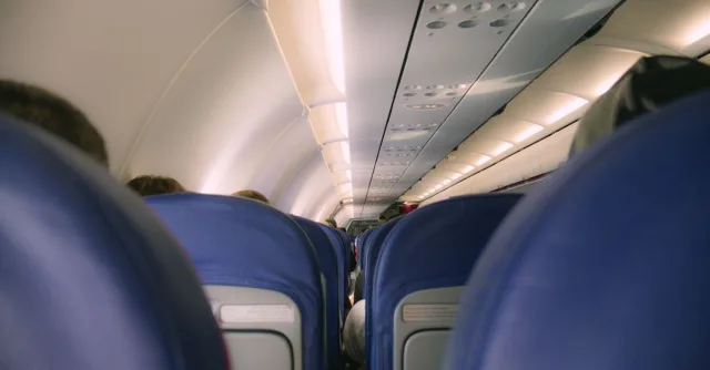 A view of a modern airplane cabin showing rows of blue seats and overhead compartments.