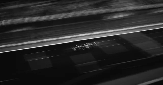 Black and white image capturing a Formula racing car on track at high speed during night race.