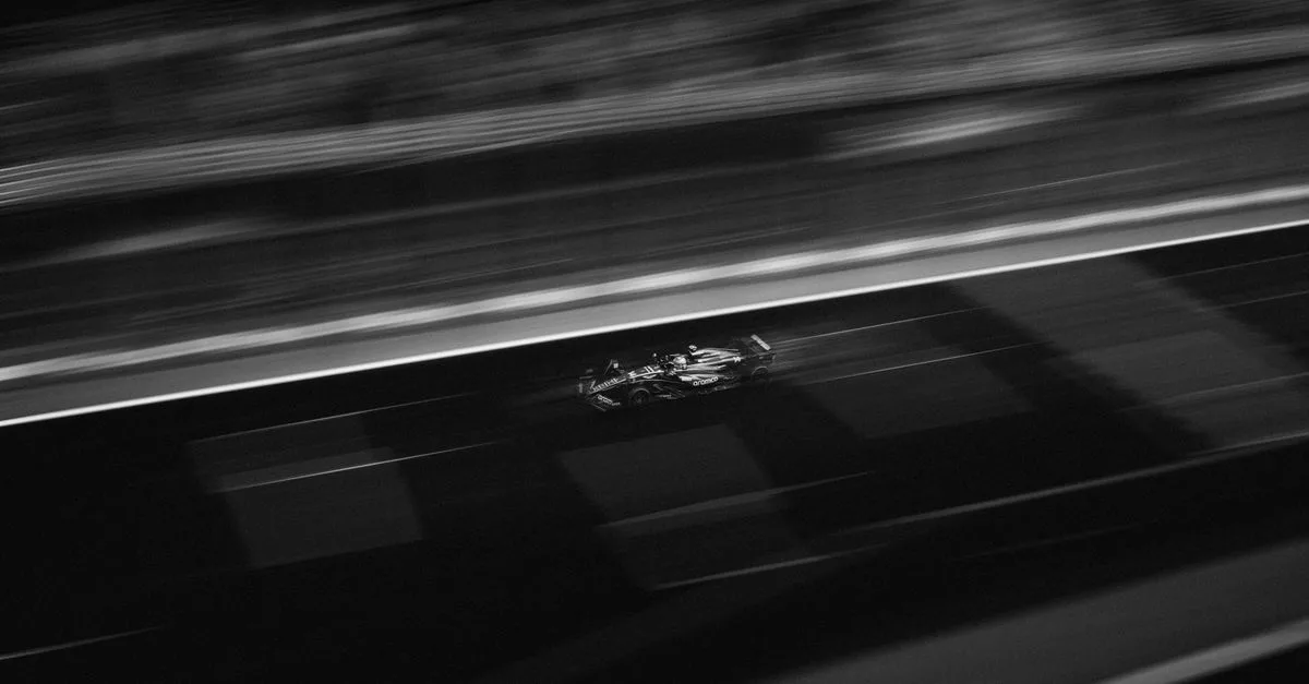 Black and white image capturing a Formula racing car on track at high speed during night race.