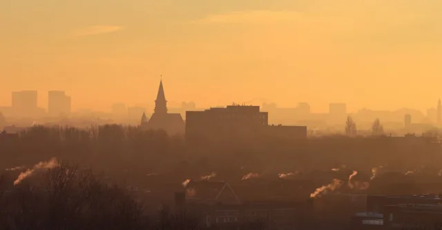 Silhouetted city skyline with mist and smoke at sunset creating a moody atmosphere.