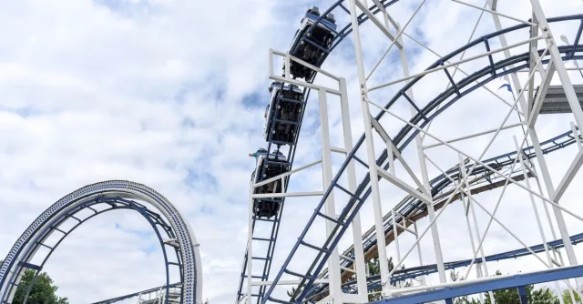 Experience the adrenaline rush of a steel roller coaster under blue skies at an amusement park.