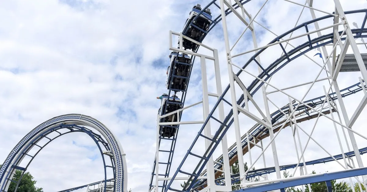 Experience the adrenaline rush of a steel roller coaster under blue skies at an amusement park.