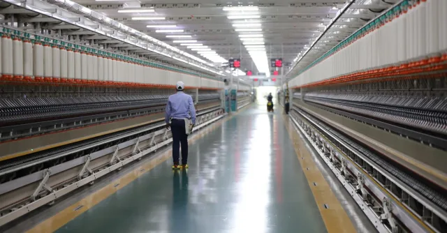 A worker walks through a wide hallway in an industrial textile plant, India.