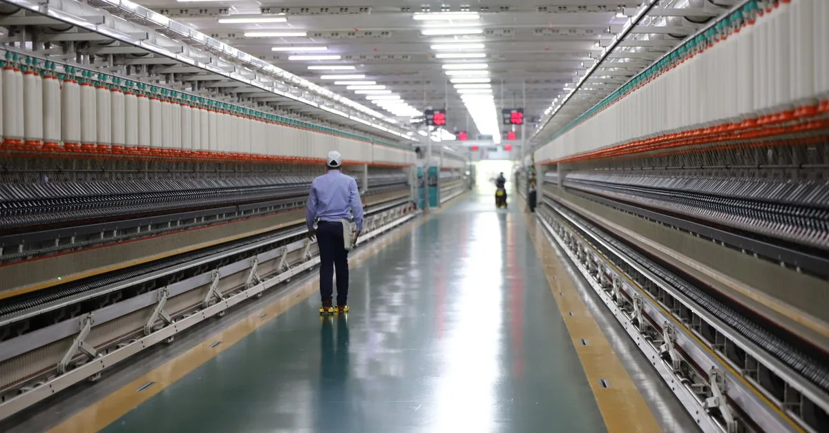 A worker walks through a wide hallway in an industrial textile plant, India.
