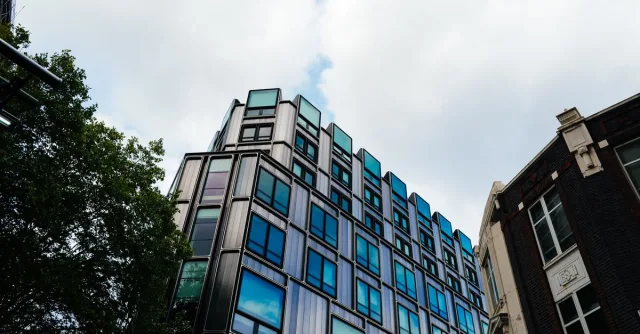 A contemporary building with reflective windows in an urban setting under a cloudy sky.