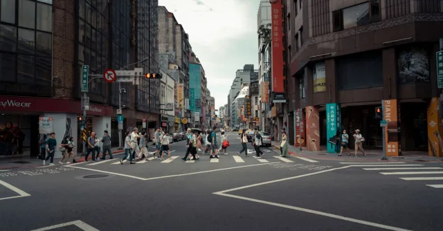 A busy urban intersection with people crossing surrounded by modern buildings, showcasing city life.