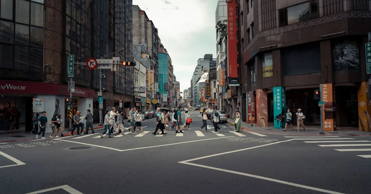 A busy urban intersection with people crossing surrounded by modern buildings, showcasing city life.