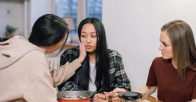 Three women at a table offering emotional support and comfort to a friend, fostering compassion and empathy.