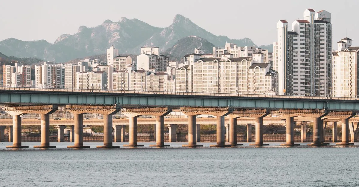 Scenic view of modern Seoul skyline with a bridge crossing the Han River and mountains in the background.