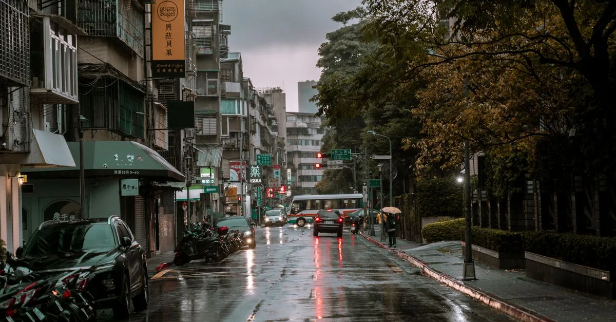 A rainy day on a bustling urban street with cars, pedestrians, and wet pavement.