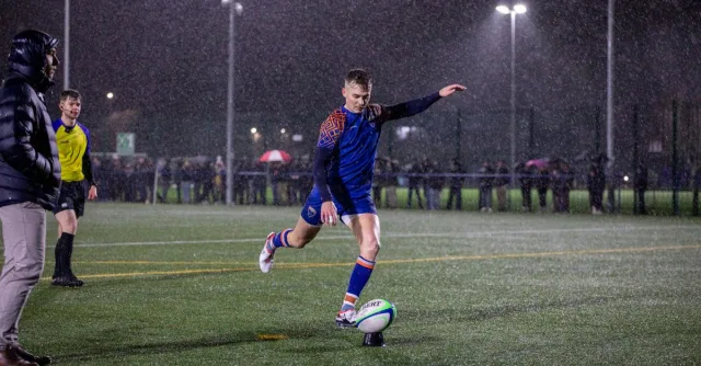 Dynamic shot of a rugby player kicking the ball during a night match in the rain at a Manchester stadium.