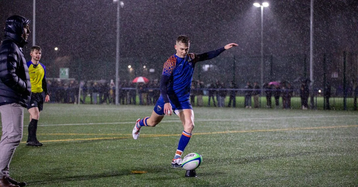 Dynamic shot of a rugby player kicking the ball during a night match in the rain at a Manchester stadium.