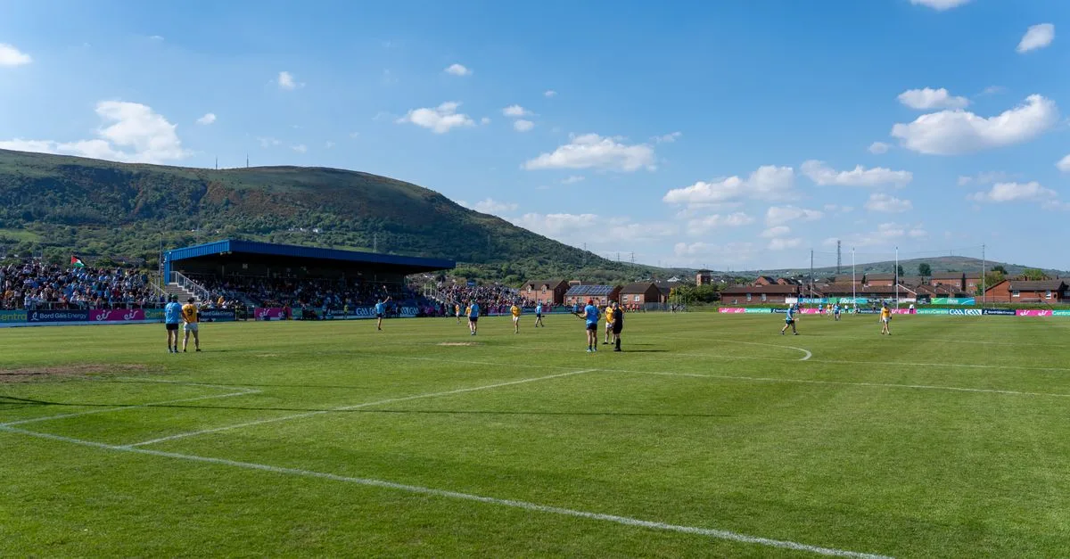 A lively Gaelic football match under blue skies with scenic hills in Ireland.