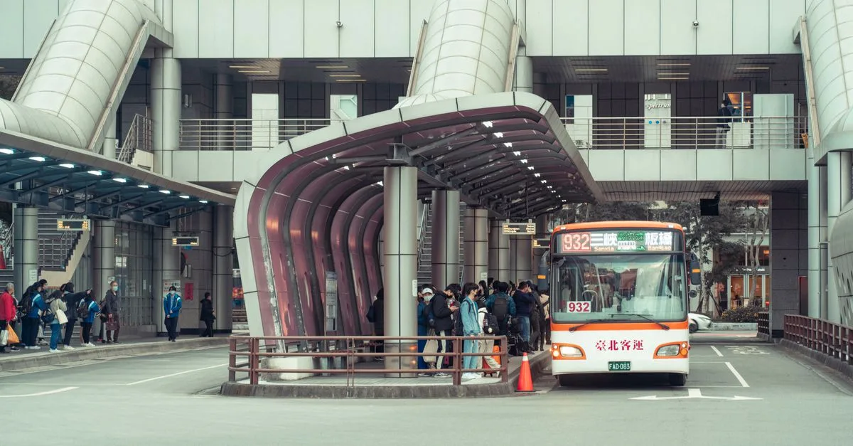 Public transport bus picking up commuters at a modern urban terminal with architectural features.