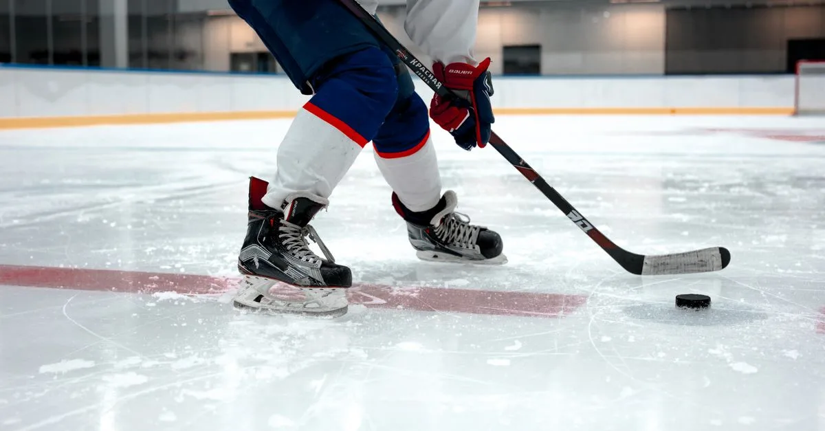 Focused ice hockey player on rink with puck and stick, showcasing agility and sports gear.