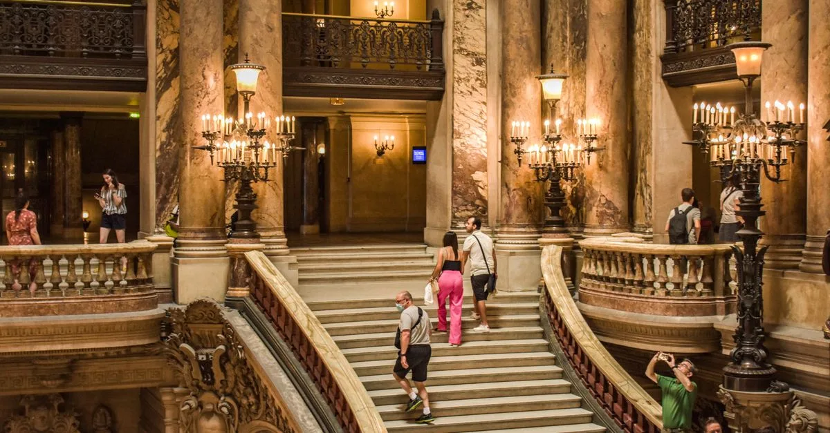 A view of the grand staircase inside Palais Garnier, showcasing its opulent architecture and tourists.