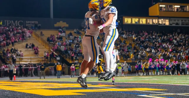 Football players celebrating during a thrilling nighttime game at a packed stadium.