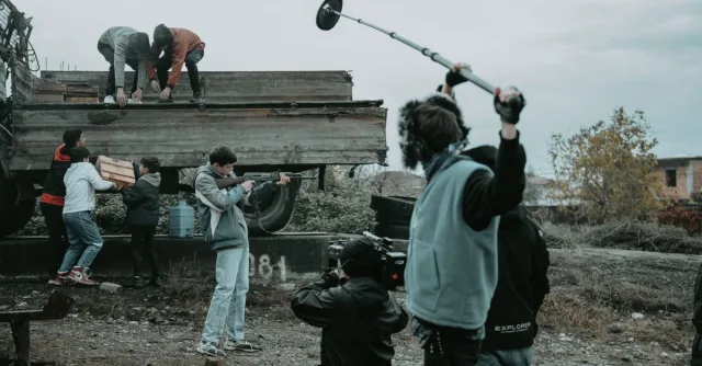 Film crew working outdoors, capturing scenes with camera and boom mic.