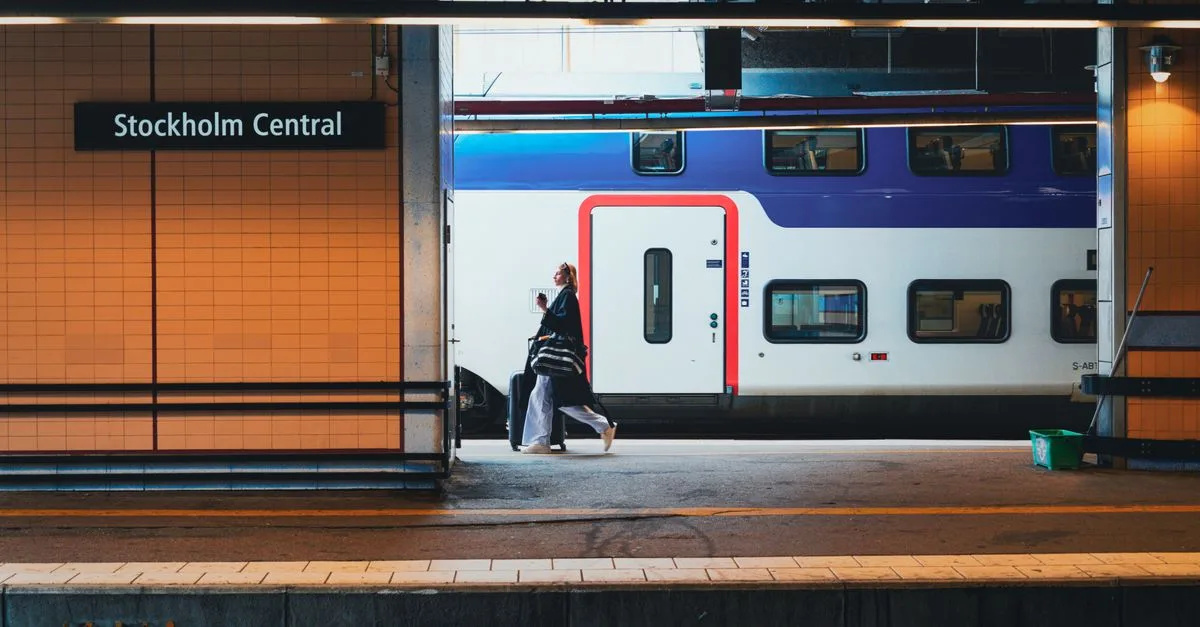 Woman walking with luggage at Stockholm Central Station's platform, beside a train.