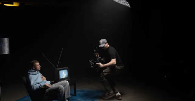 A photographer captures a scene with a man sitting next to an old TV in a dimly lit studio.
