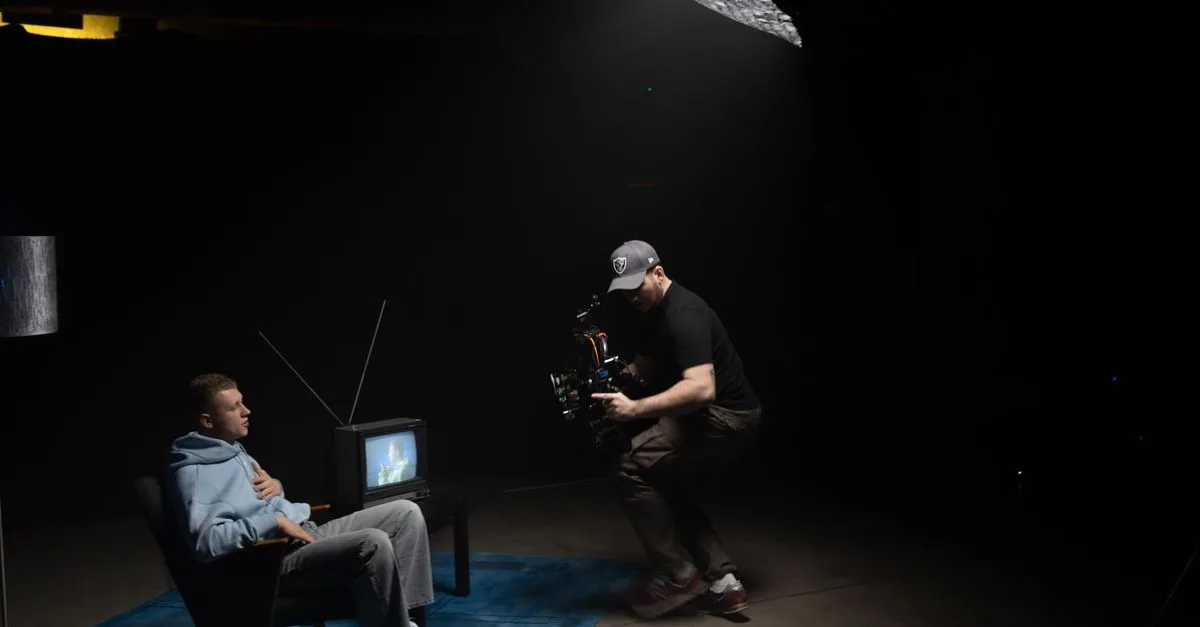 A photographer captures a scene with a man sitting next to an old TV in a dimly lit studio.