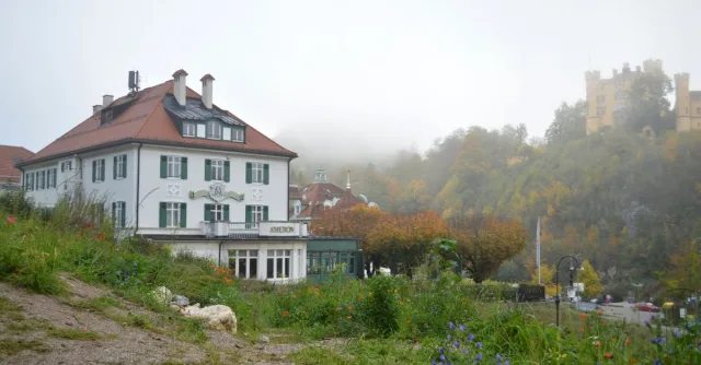 Picturesque view of a Bavarian hotel and foggy castle surrounded by autumn foliage.