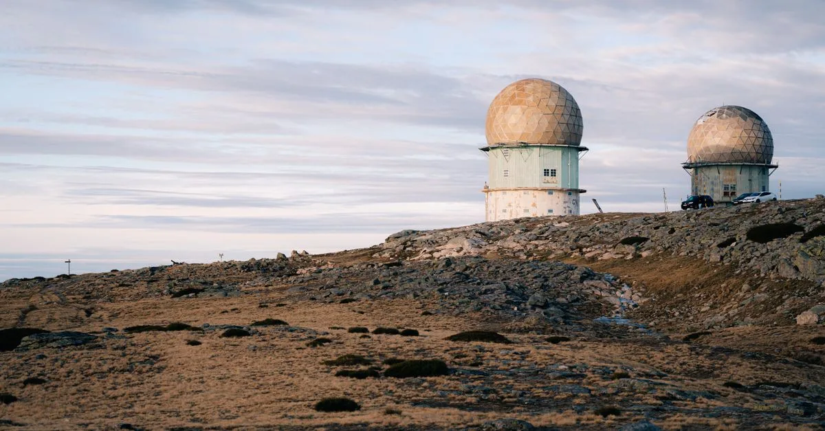 Two radar domes on a rocky landscape under a cloudy twilight sky, symbolizing technology and isolation.