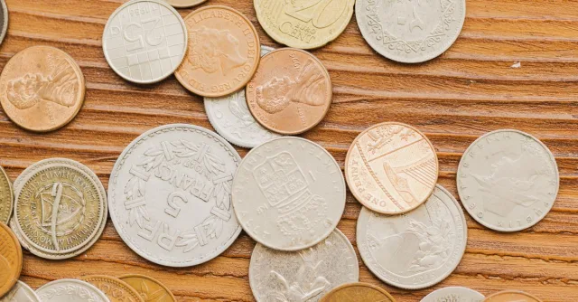 A collection of diverse vintage coins scattered on a wooden surface, showcasing international currency designs.