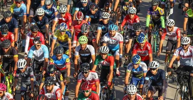 Large group of cyclists in vibrant jerseys race on Blida streets during a sunny day, capturing the essence of intense road cycling.
