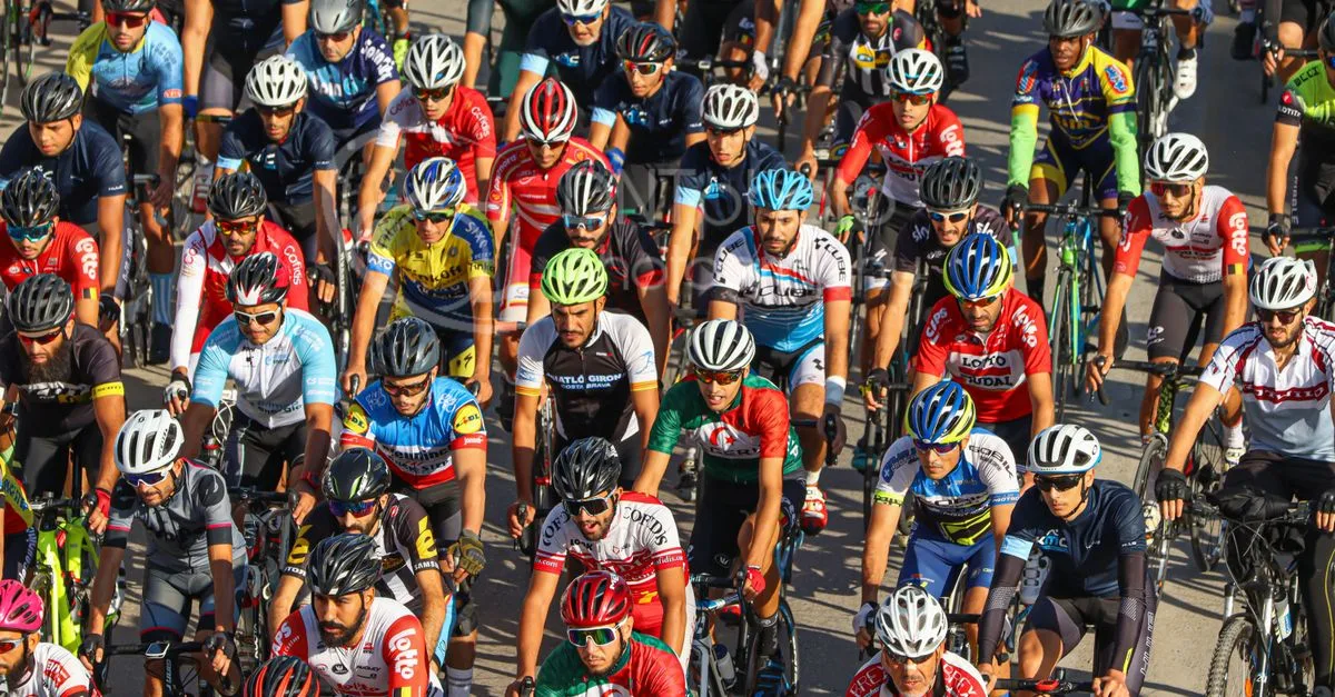 Large group of cyclists in vibrant jerseys race on Blida streets during a sunny day, capturing the essence of intense road cycling.