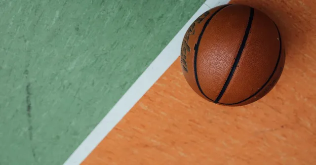 A close-up of a basketball resting on a colorful court with orange and green sections.