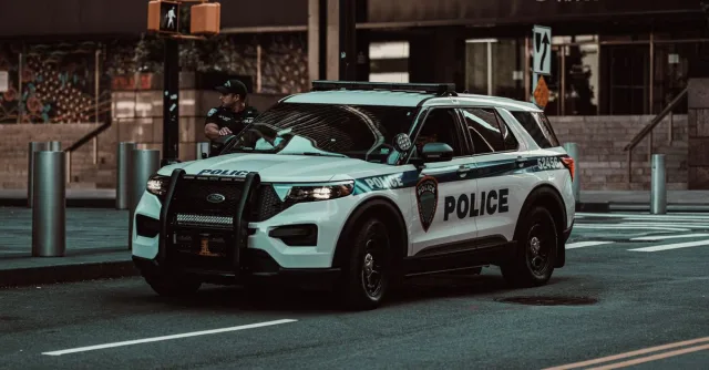 A police car parked on a street in New York City with a policeman nearby, showcasing urban safety.