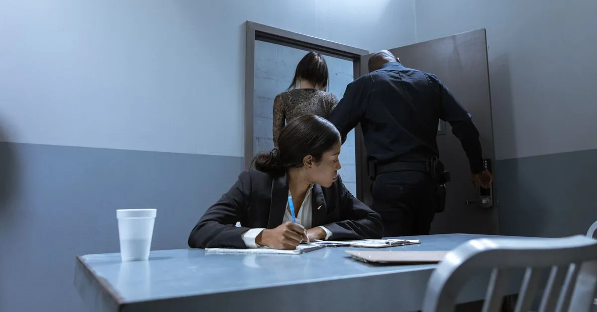 Police officer escorting suspect as lawyer observes during interrogation.