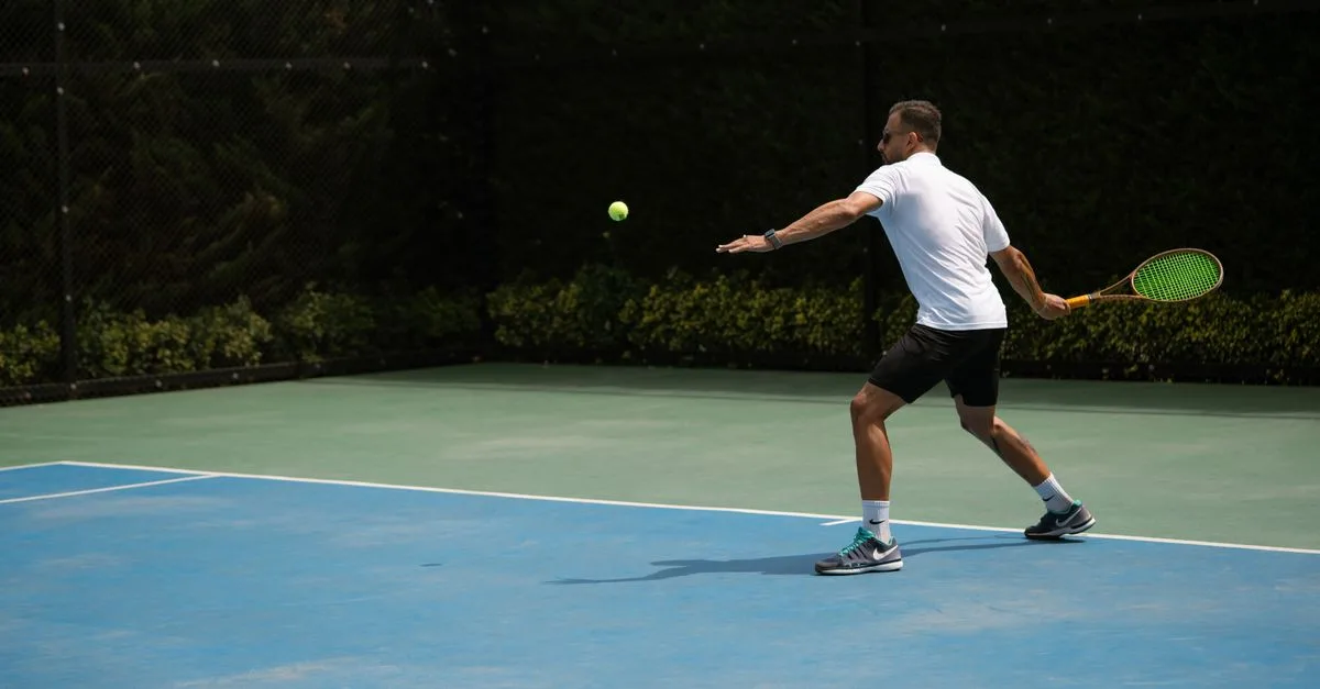 Tennis player hitting a backhand shot on a sunny outdoor court in Iran.