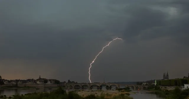 A powerful lightning strike illuminates a stormy sky over a historic bridge, capturing nature's raw power.