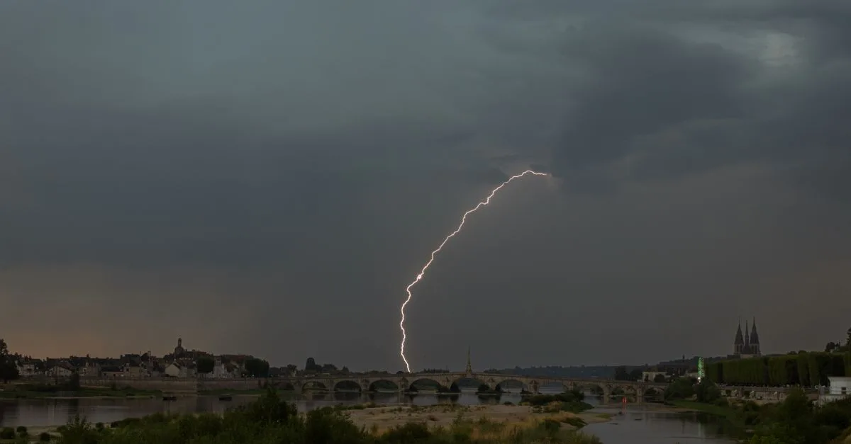 A powerful lightning strike illuminates a stormy sky over a historic bridge, capturing nature's raw power.