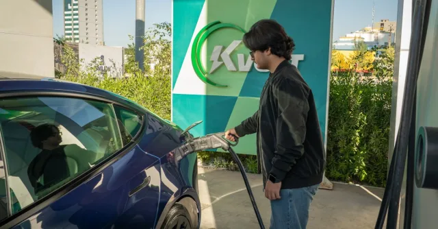 Young man charging a Tesla Model 3 at an outdoor electric vehicle station during the day.