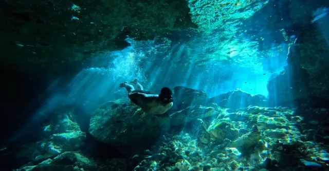 Diver exploring an underwater cave with stunning light beams and vibrant blue hues.