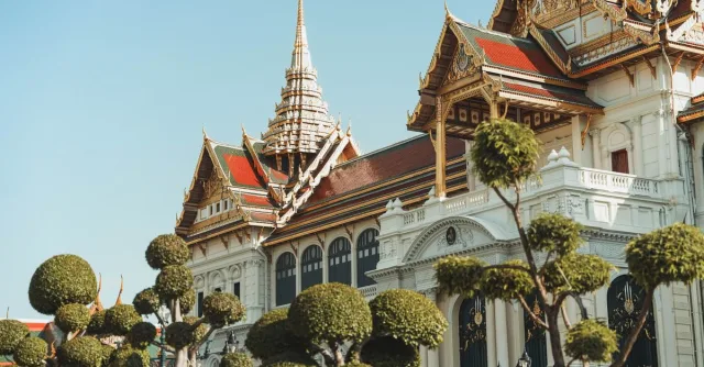 Stunning view of the Grand Palace's ornate architecture with trimmed trees in Bangkok, Thailand.