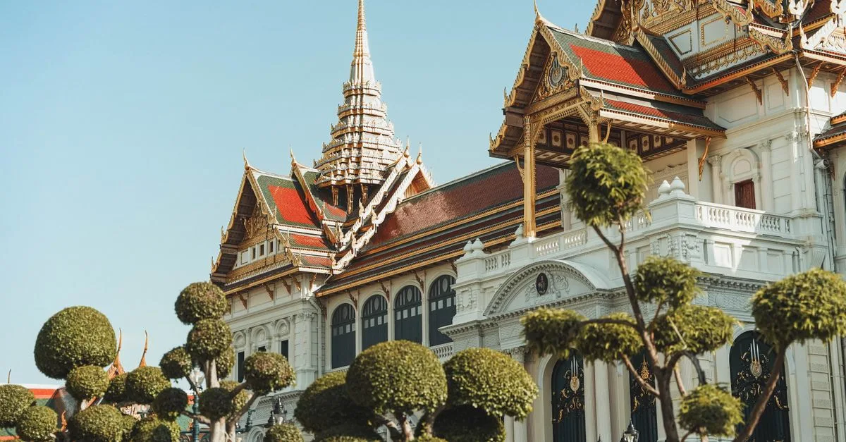 Stunning view of the Grand Palace's ornate architecture with trimmed trees in Bangkok, Thailand.