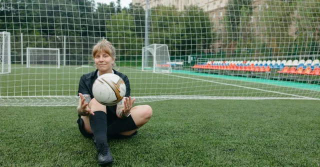 A female soccer player sitting with a ball on a soccer field, enjoying a break.