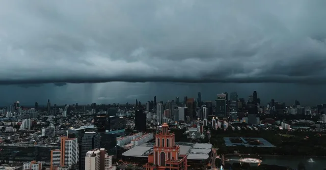 Aerial view of Bangkok's urban skyline under dark storm clouds, capturing the city's dramatic atmosphere.