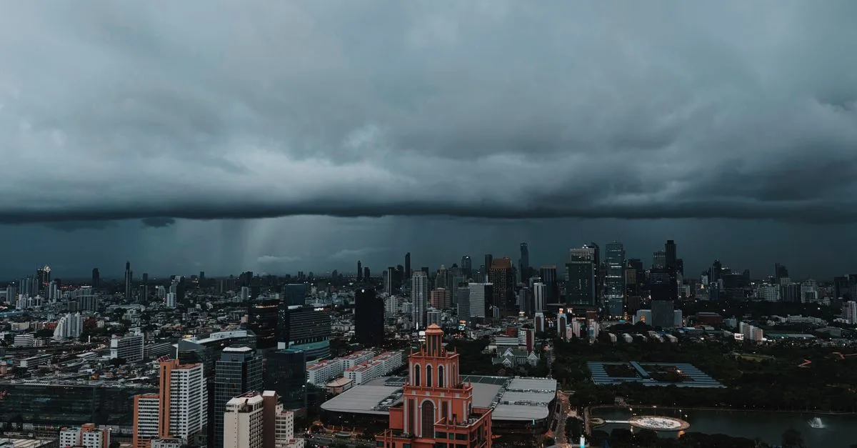 Aerial view of Bangkok's urban skyline under dark storm clouds, capturing the city's dramatic atmosphere.