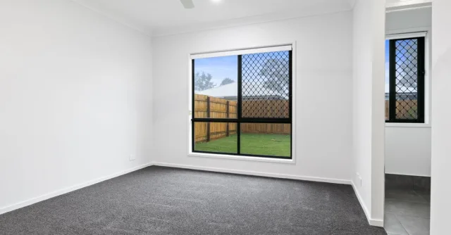 Empty room with large window and gray carpet, ideal for real estate listings.
