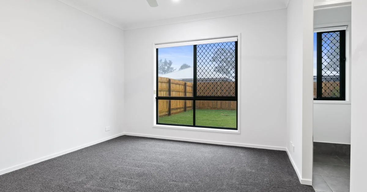 Empty room with large window and gray carpet, ideal for real estate listings.
