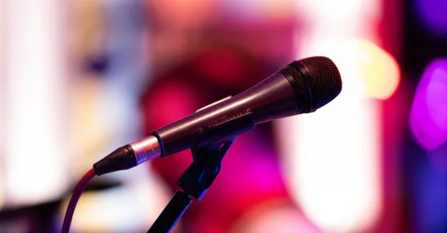 Close-up shot of a microphone on stage with colorful background bokeh, capturing live performance ambiance.