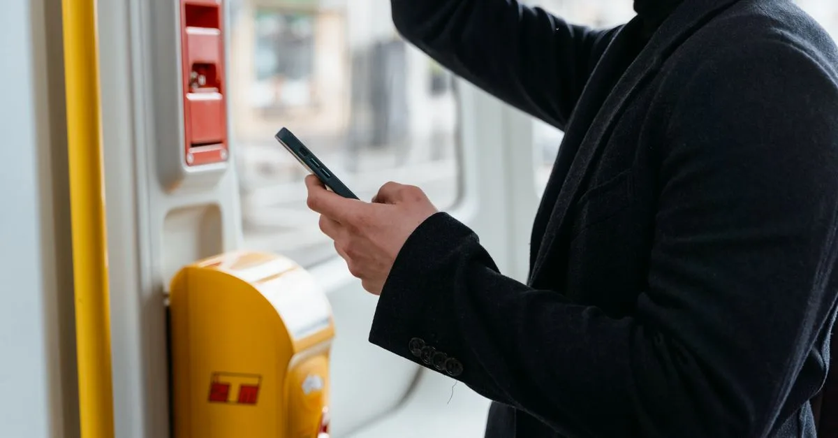 Adult in a black coat checking smartphone while commuting on public transport.